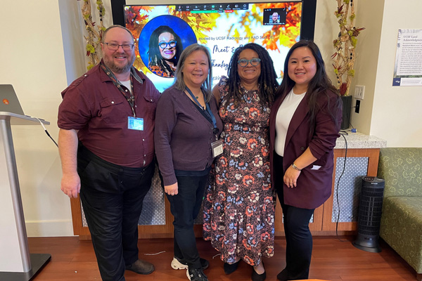 Four people standing together and smiling in front of a large digital screen