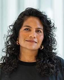 Woman with long curly black hair wearing a black top with a light filled background