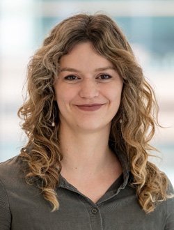 Woman with long curly blonde hair wearing a green shirt with a light background.