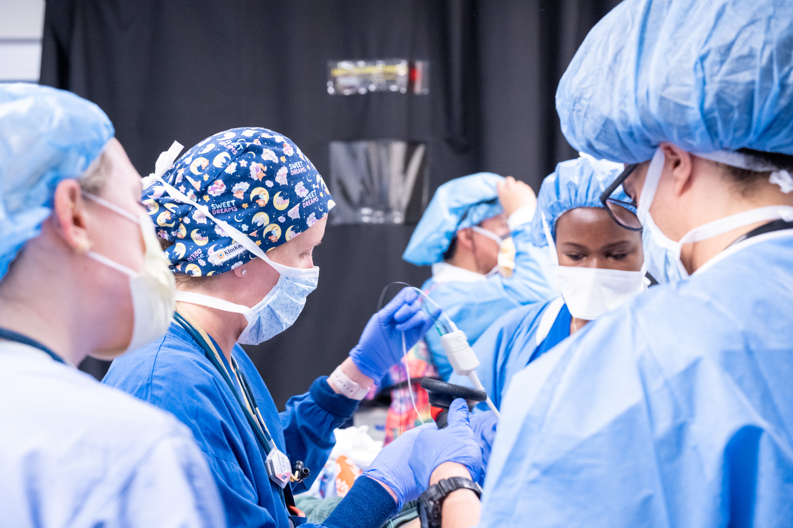 A group of medical professionals wearing scrubs, masks and head coverings working together in a clinical setting.