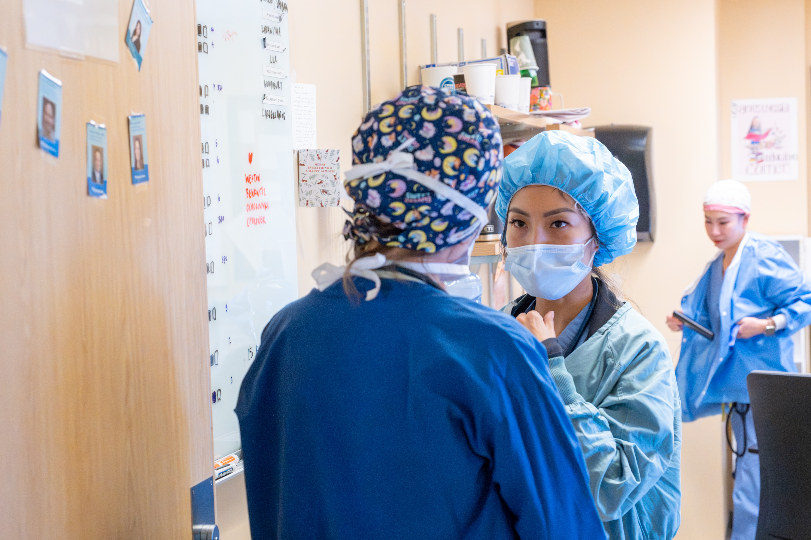 Two doctors wearing scrubs confer with each other while referring to a white board.