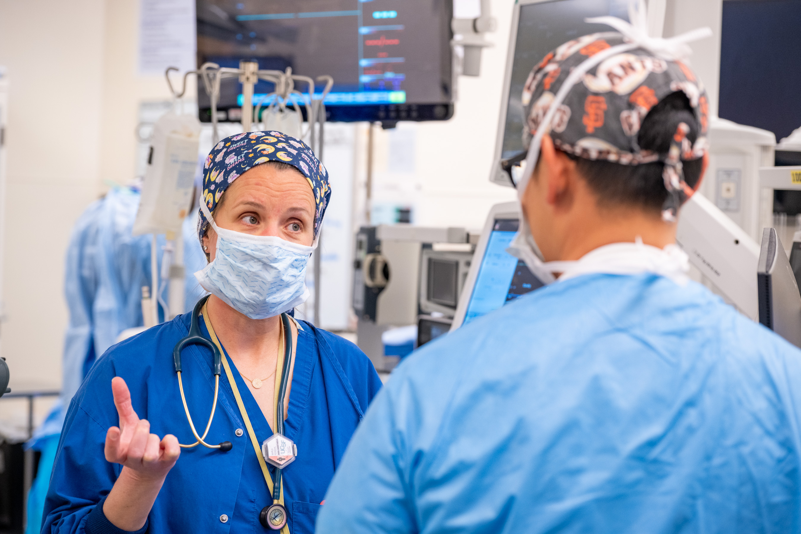 Two doctors conferring in a clinical setting each is wearing blue scrubs, masks and head coverings.