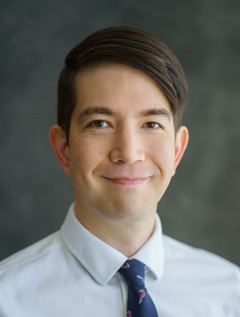 Person with short dark brown hair wearing a shirt and tie.