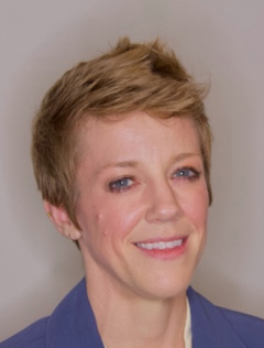Smiling person with short blonde hair wearing a blue jacket.