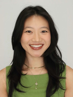 Smiling person with long black hair wearing a green top.