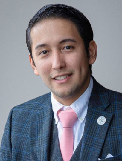 Smiling man with short black hair, wearing a gray and blue suit with a pink tie.