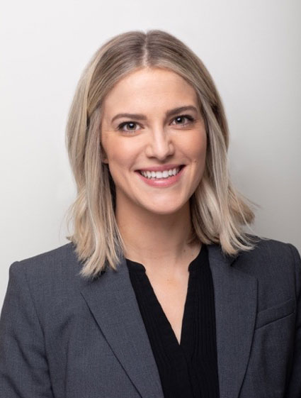 Smiling woman with shoulder length blonde hair, wearing a gray jacket over a black shirt.