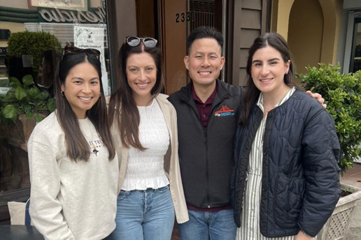 four people smiling outside in front of a business