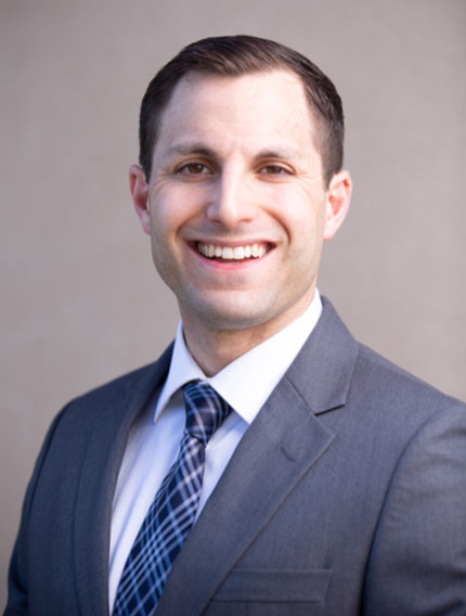 Smiling man with short brown hair, wearing a gray suit and blue tie.