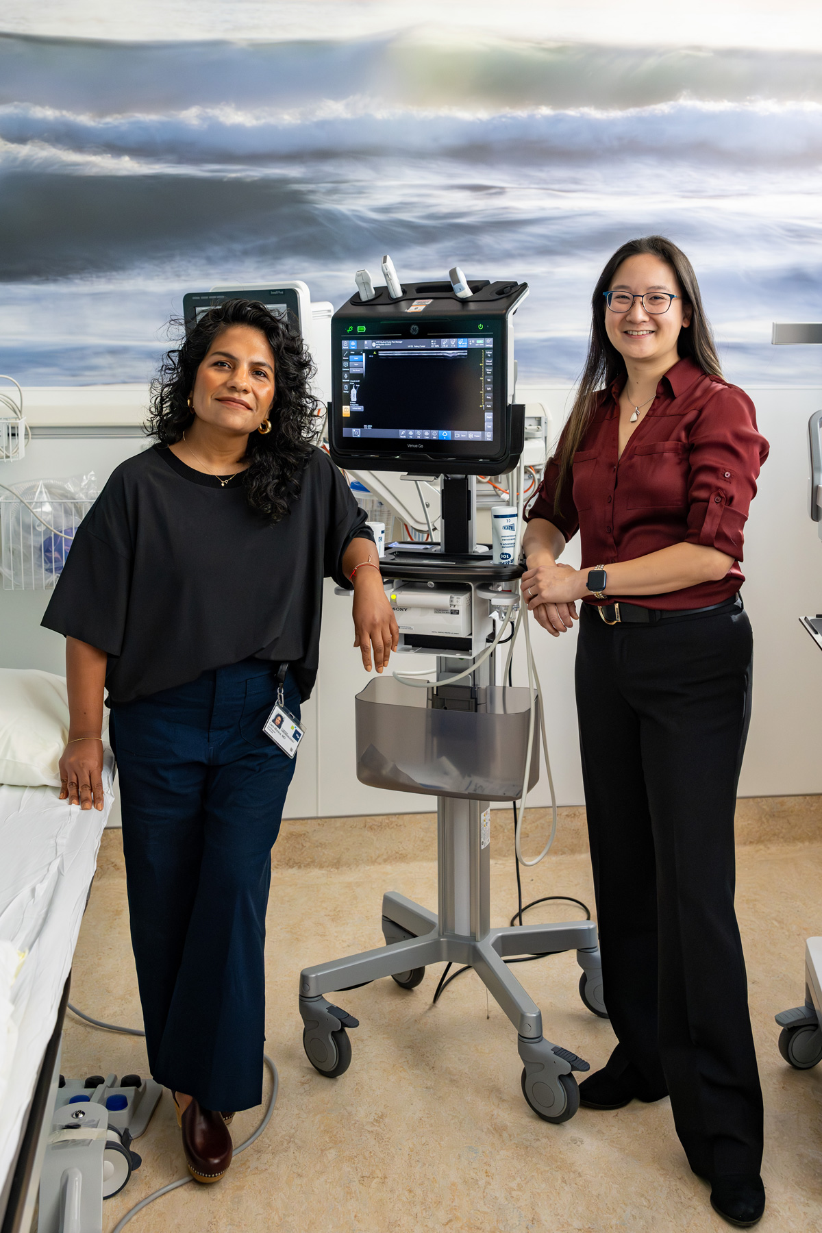 Two woman standing in a clinical room with an imaging device and a full size ocean scape mural on the wall behind them