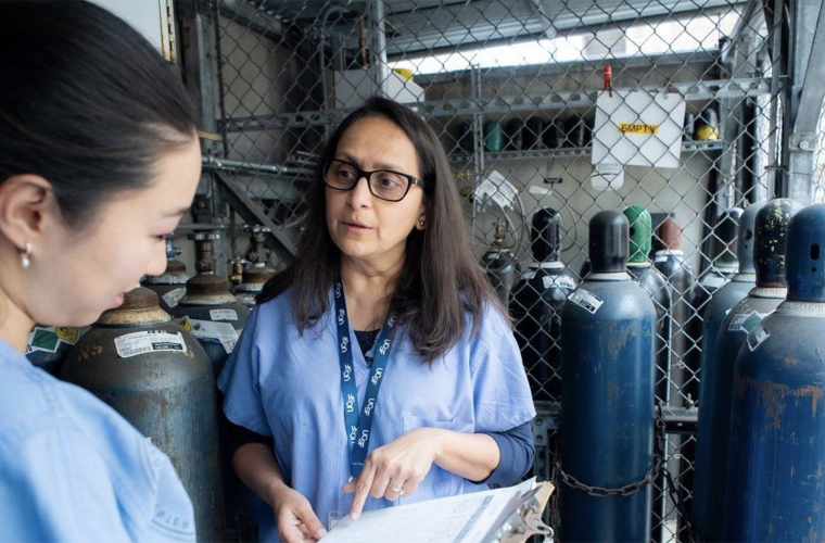 Two women wearing blue medical scrubs discussing something on a clipboard.