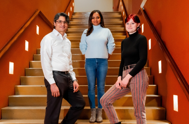 Three smiling people standing in a red walled stairway