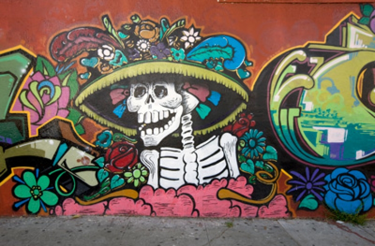 A large colorful day of the dead themed mural on a wall, featuring a skeleton.