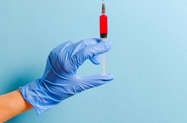 a gloved hand holding a syringe filled with red liquid
