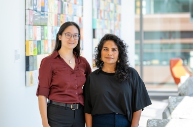 Two woman standing side by side in front of a large tiled artwork.