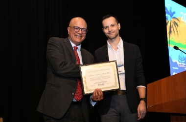 Two men stand near a podium holding a framed certificate.