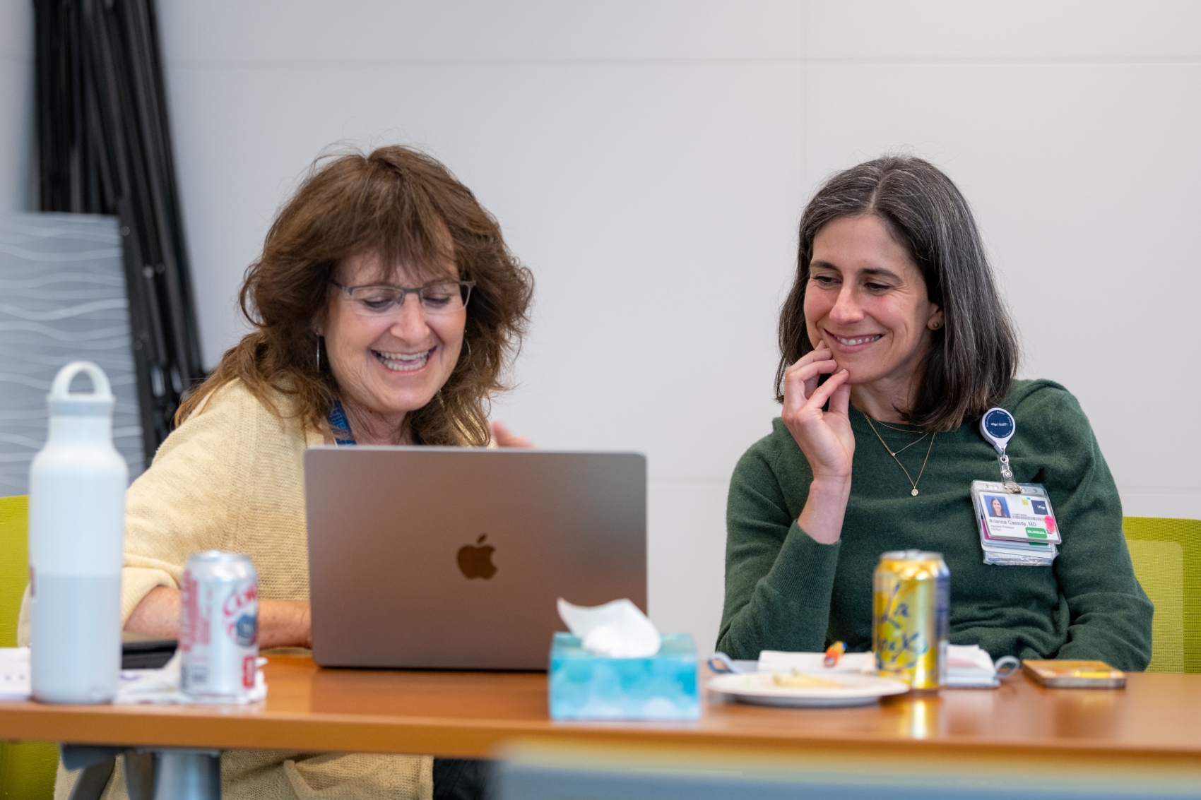 Two woman with long brown hair smiling while looking at a computer together.