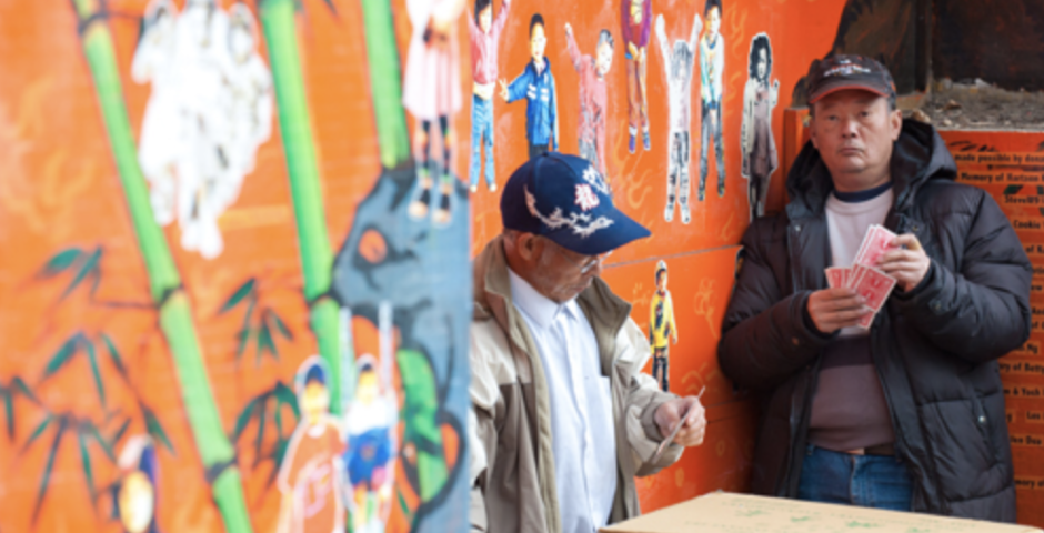 two men leaning on orange wall