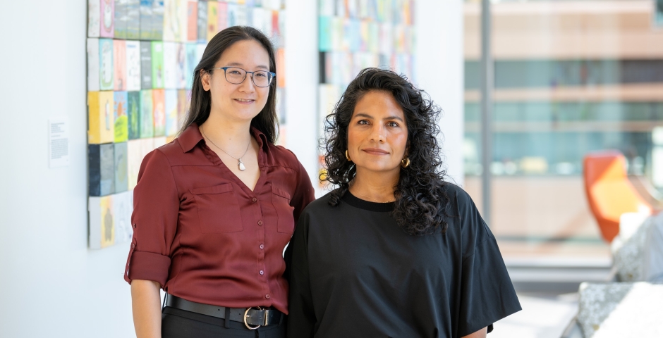 Two woman standing side by side in front of a large tiled artwork.