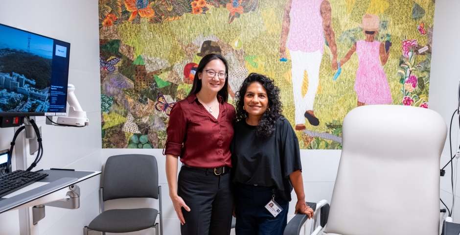 Two woman standing together in a medical exam room featuring a full size wall mural on one wall.