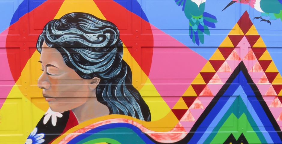 A colorful mural painted on a garage door featuring a woman and two hummingbirds with a colorful geometric design.
