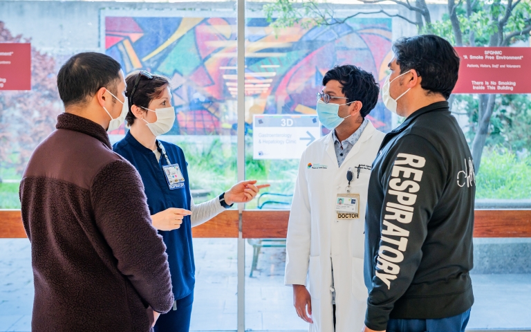 A doctor talks with three respiratory therapists in front of a mural