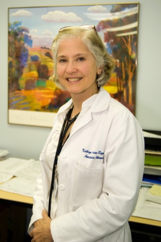 Woman smiling and wearing a white lab coat with the a painting in the background.