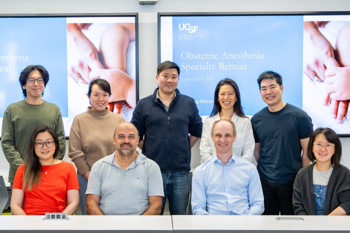 A group of nine people posing in front of large slides for the Obstetric Anesthesia Specialty Retreat.