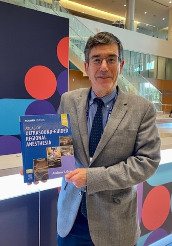 Man with short salt and pepper hair wearing glasses and a suit and tie holding a book.
