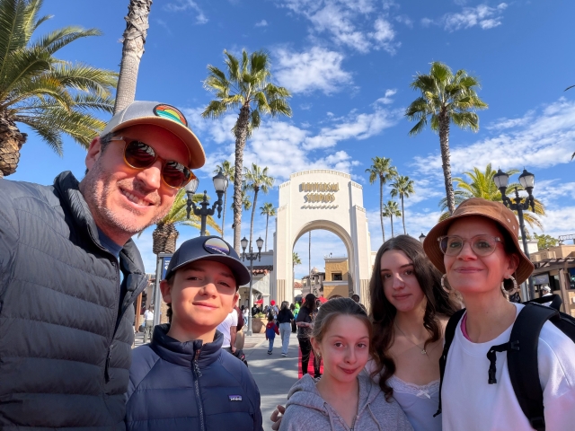 A selfie of a family of five at Universal Studios with palm trees and blue skies in the background.
