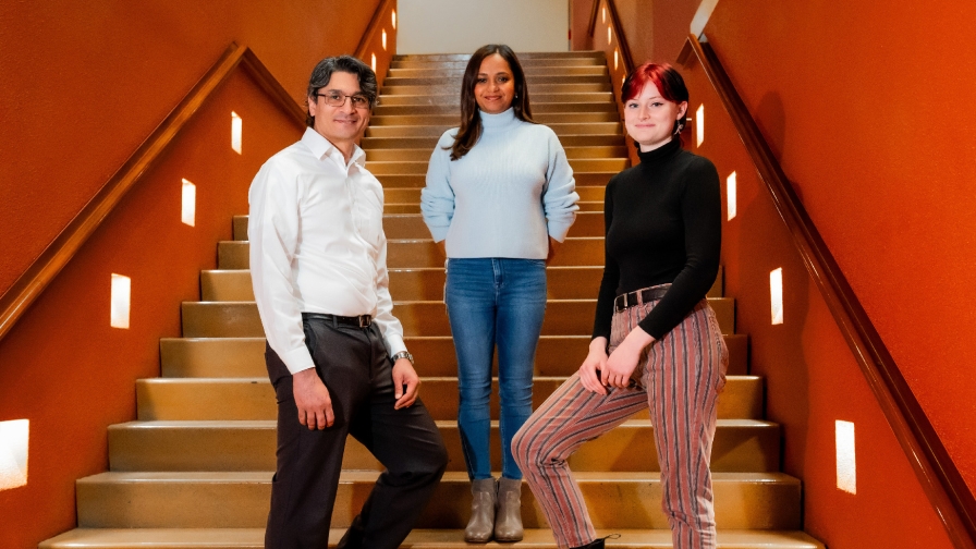 Three smiling people standing in a red walled stairway