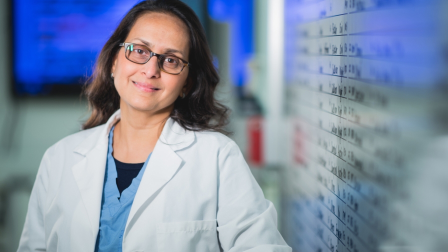 Woman with glasses and long brown hair wearing a white lab coat in a clinical setting