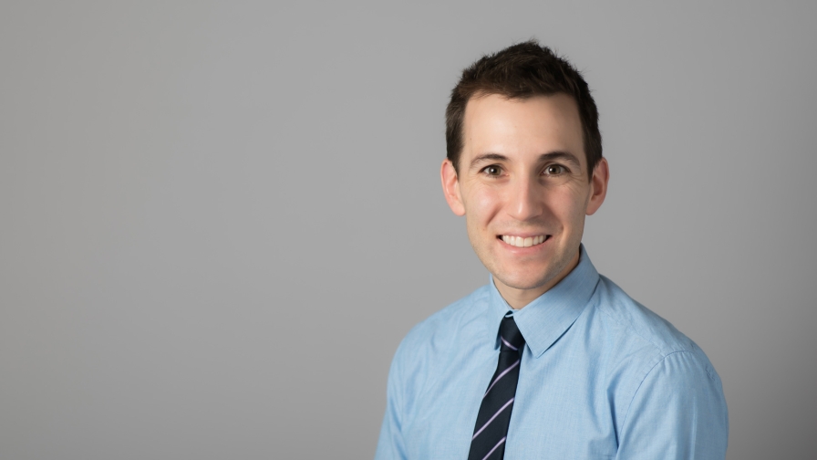 Man with dark short hair, wearing a light blue shirt and a tie.