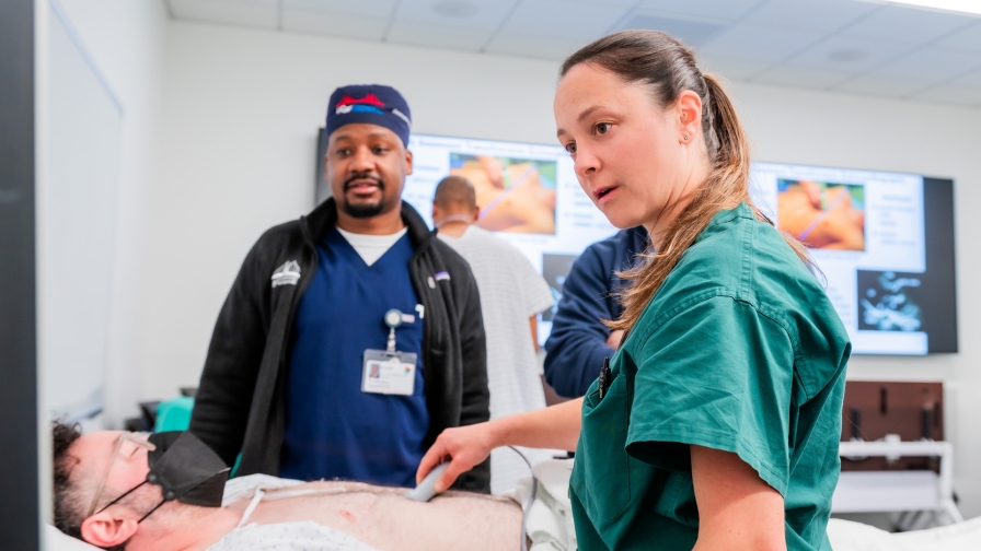 two people in scrubs standing over a patient wearing a mask in a clinical setting