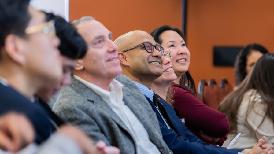 Several members of an audience seated and looking up at a presentation while smiling.