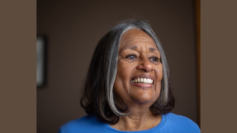 Woman with sliver and black hair smiling and looking into the distance wearing a blue sweater with a dark background