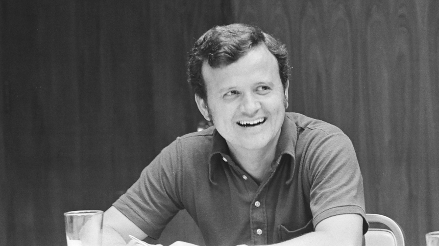 Man smiling with short dark hair wearing a polo shirt seated at a table.