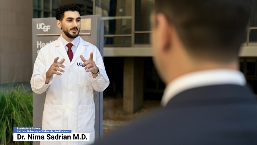 Man in a white UCSF lab coat standing outside delivering remarks to another person.