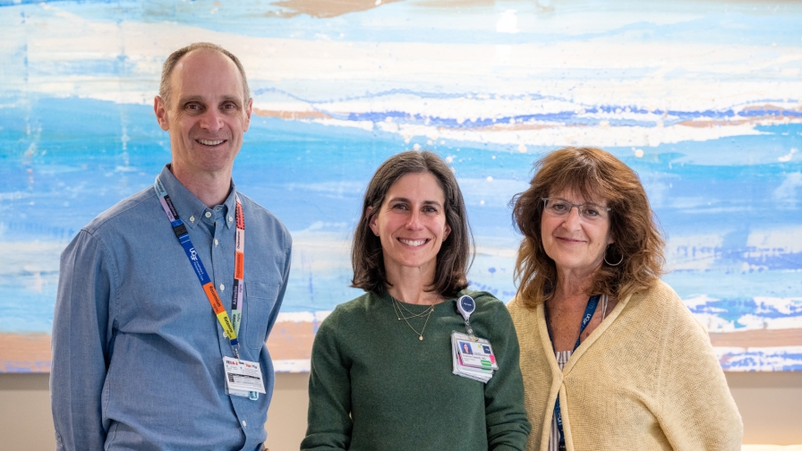 Three people standing together and smiling in front of an abstract blue painting.