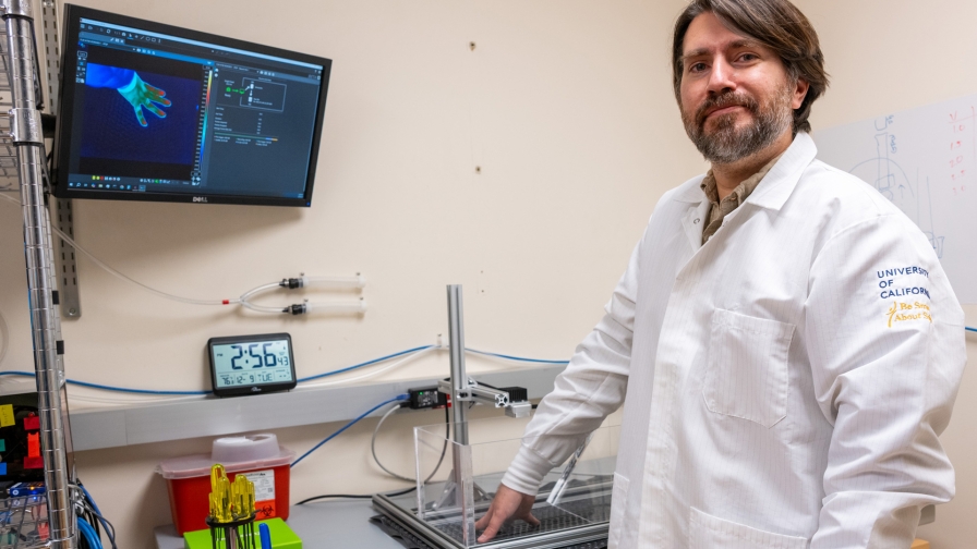 A man with short brown hair wearing a white lab coat places his hand on a device and looks at a monitor that displays the pressure of his hand on the device.