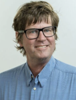 A man wearing a blue collard shirt and glasses