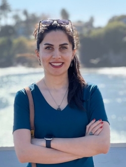 woman in a blue shirt smiling in front of water.