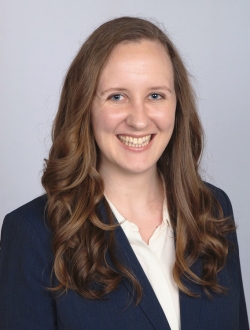 Woman with long brown wavy hair and a dark blazer smiling