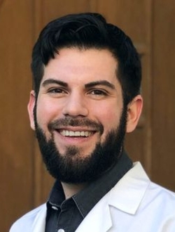 Bearded man with short dark hair, wearing a lab coat and smiling