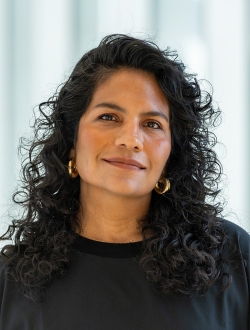 Woman with dark curly hair and a dark shirt with a light and airy background