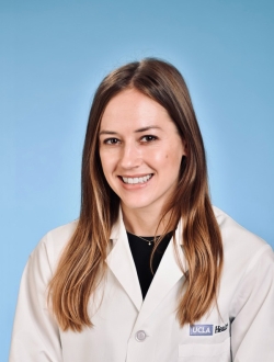 Smiling woman, with long brown hair wearing a white lab coat