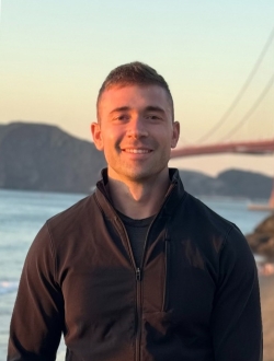 Person with short hair smiling with part of the Golden Gate Bridge in the background