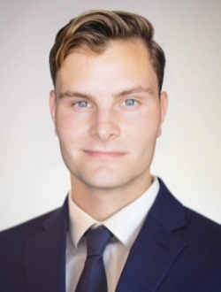 Man with short blond hair wearing a navy blue suit and tie