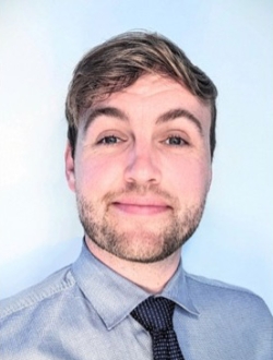 Man with short blond hair wearing a light gray shirt and dark tie