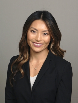 Smiling woman with dark long hair and a dark jacket in front of a grey background